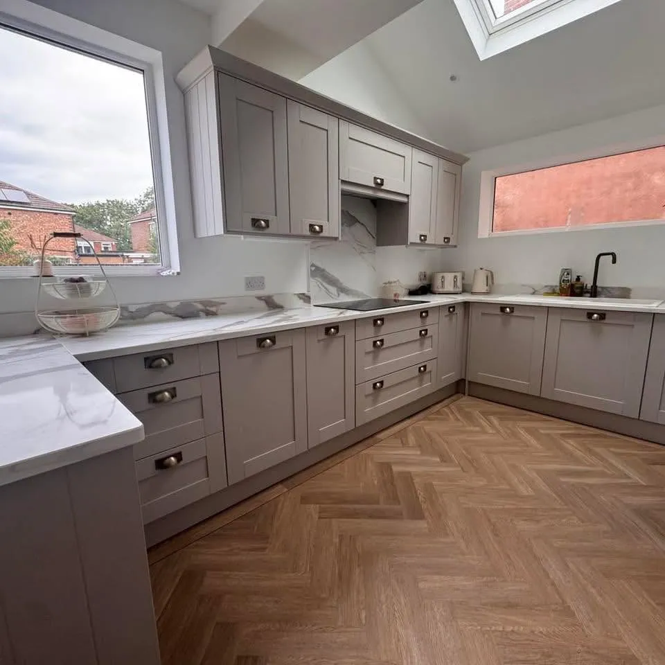 A kitchen completed by J&J, with grey fitted cabinets, pale worktops and herringbone flooring